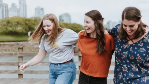 Three women on a bridge, laughing and smiling