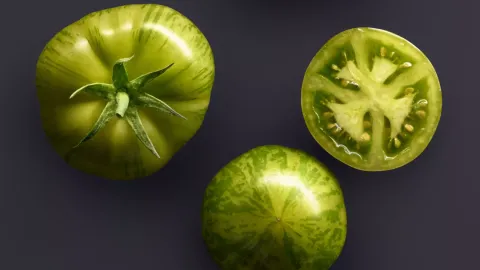 Three green tomatoes on a dark grey background